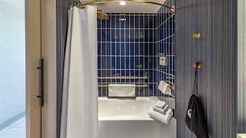 A modern bathroom with a bathtub, a shower with a gold shower head, and a towel rack with multiple towels.
