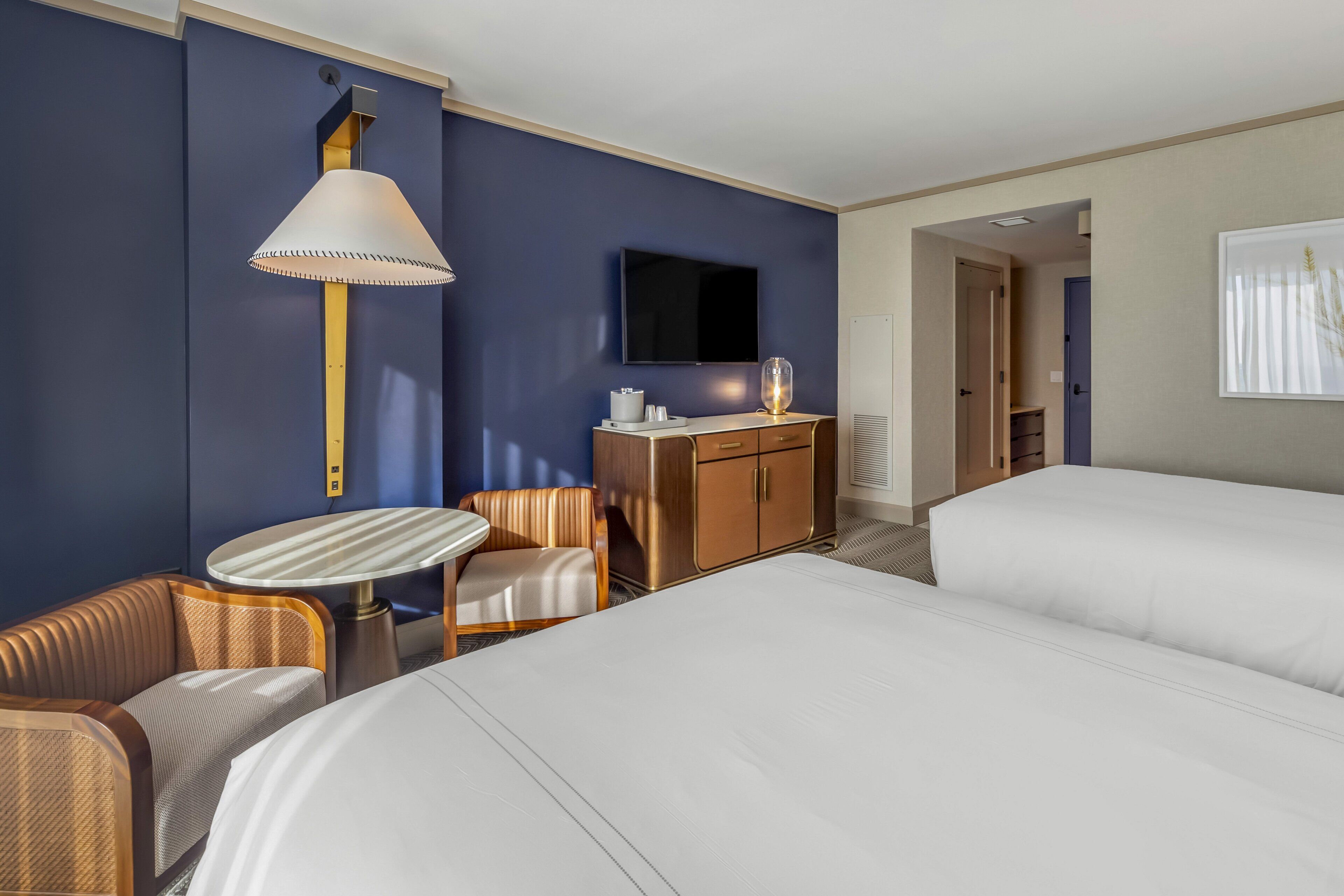 A hotel room with a bed, a desk with a lamp, a television, and a seating area.
