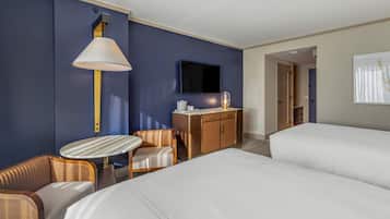 A hotel room with a bed, a desk with a lamp, a television, and a seating area.