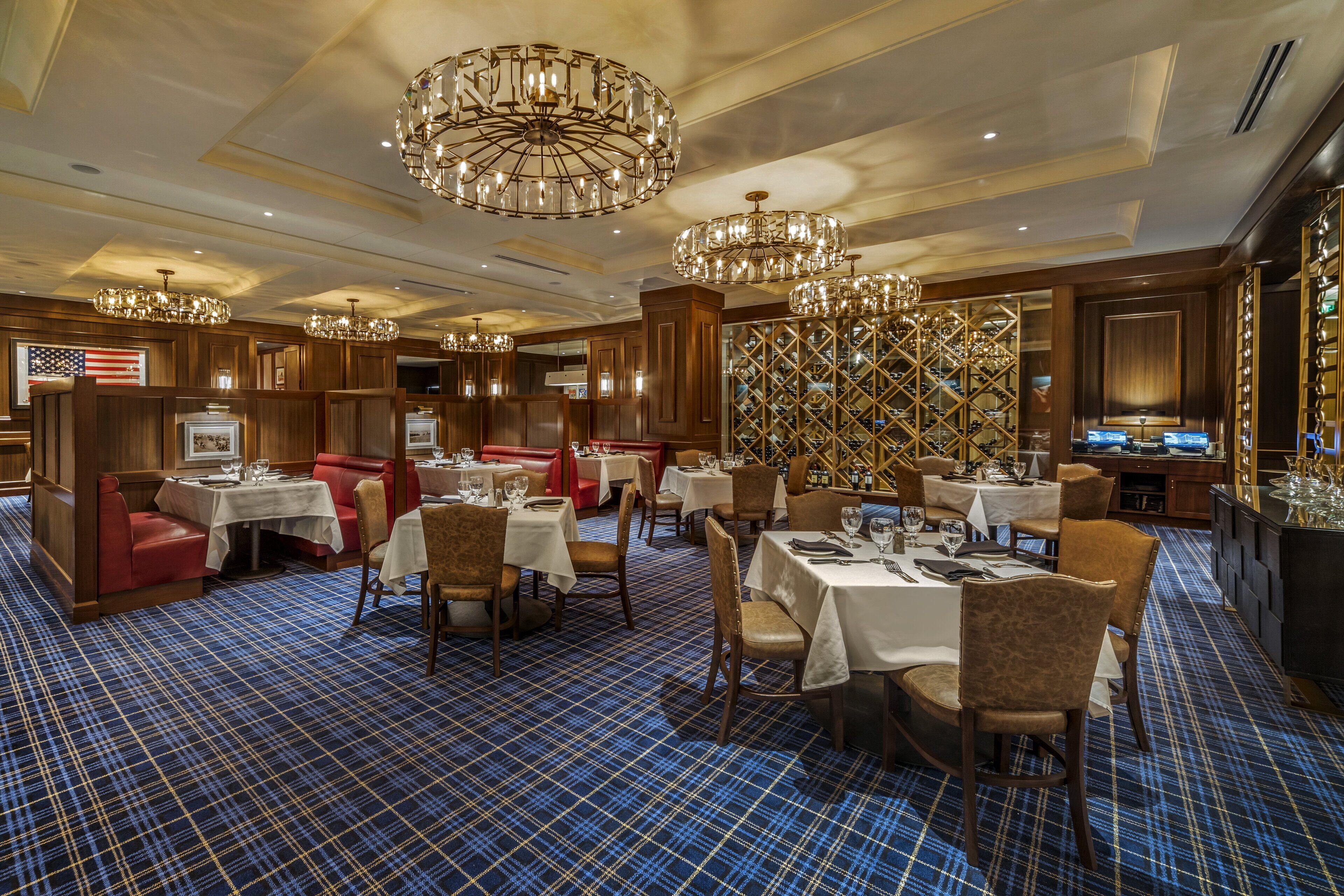 A restaurant with multiple dining areas, including booths and tables, with a blue plaid carpet and chandeliers.