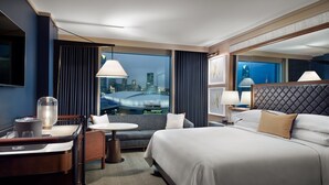 Una habitación de hotel con una cama grande, un escritorio con lámpara, una silla y vistas a un paisaje urbano.