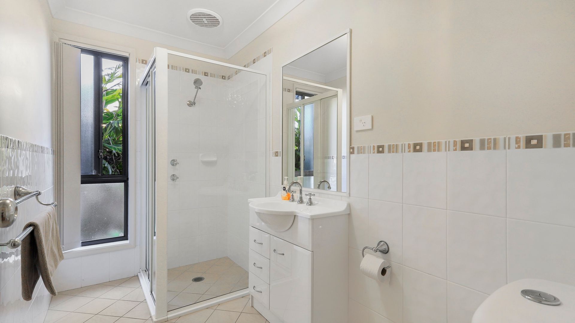 Un baño moderno con cabina de ducha de vidrio, un lavabo blanco con espejo y un inodoro.
