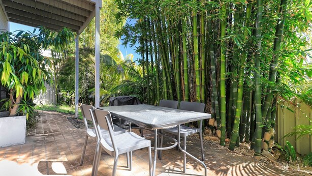 An outdoor patio with a metal table and chairs, surrounded by bamboo plants and other greenery. - Sea Change on Excellent (Vincentia)