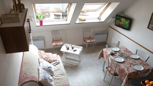 A cozy loft apartment with a dining area, a sofa, and a TV mounted on the wall. - Duplex T3 in Luchon - 6 pers, cable car, parking, wifi (Bagnères-de-Luchon)