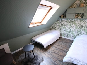 Ein Schlafzimmer mit schrägem Dach, einem Oberlicht, einem Bett, einem kleinen runden Tisch und einem Schrank mit Dekorationsgegenständen.