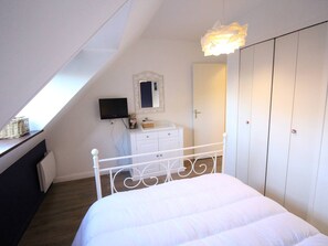A bedroom with a sloped ceiling, a bed with white bedding, a dresser, a television, a mirror, and a wardrobe. - Duplex T3 in Luchon - 6 pers, cable car, parking, wifi (Bagnères-de-Luchon)
