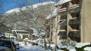 A building with multiple balconies and a parking area with snow-covered surroundings. - Duplex T3 in Luchon - 6 pers, cable car, parking, wifi (Bagnères-de-Luchon)