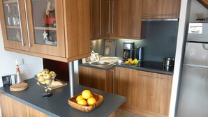 A modern kitchen with wooden cabinets, a stainless steel refrigerator, and a countertop with a bowl of apples and oranges. - Duplex T3 in Luchon - 6 pers, cable car, parking, wifi (Bagnères-de-Luchon)