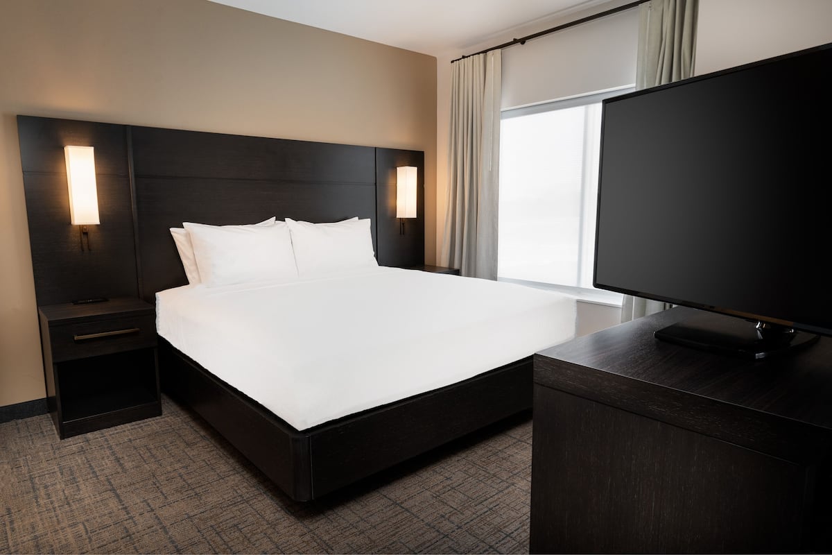 Una habitación de hotel con una cama grande, un televisor de pantalla plana y dos mesitas de noche con lámparas.