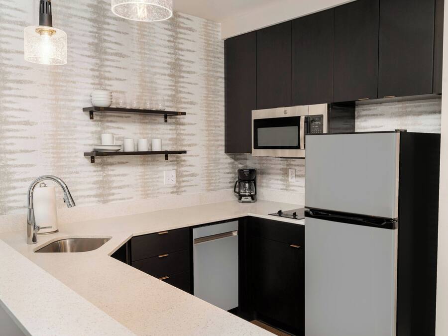 A modern kitchen with a stainless steel sink, black cabinets, a microwave, and a refrigerator.