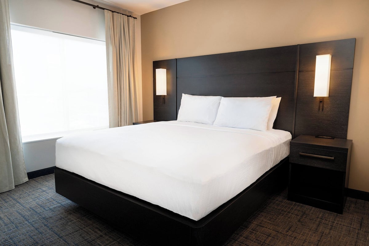 Una habitación de hotel con una cama grande, dos mesitas de noche y una ventana con cortinas.