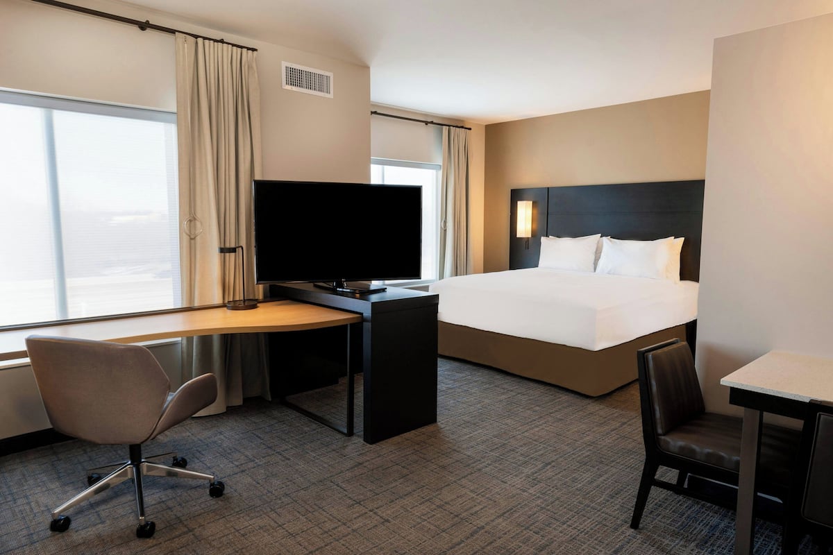 Una habitación de hotel con cama, escritorio, silla, televisor y ventana con cortinas.