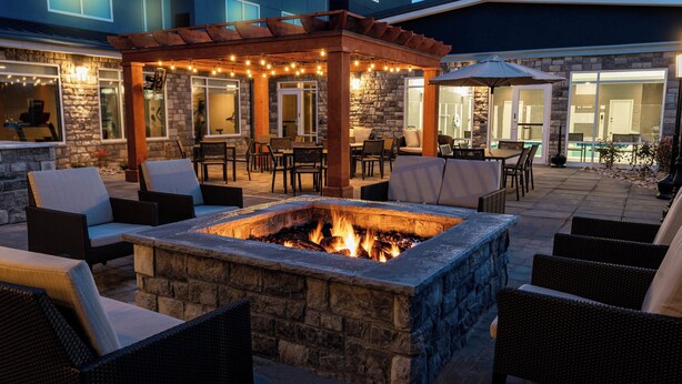 Un patio exterior con un hogar de piedra, muebles de mimbre e iluminación de guirnaldas.