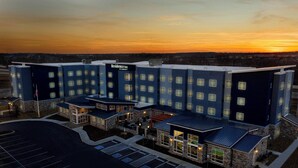 Un hotel de varios pisos con techo plano, estacionamiento y una vista despejada del atardecer al fondo.