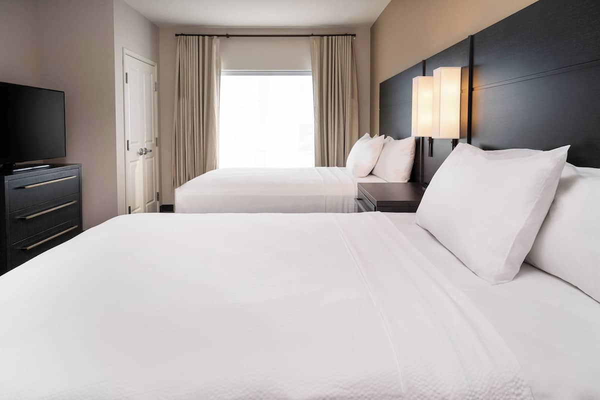 Habitación de hotel con dos camas, televisión, cómoda y ventana con cortinas.