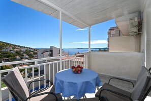 A balcony with a table and chairs, overlooking a coastal town and the sea.