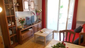 Un salon chaleureux avec un meuble en bois, un téléviseur et une table à manger agrémentée d’un vase de fleurs.
