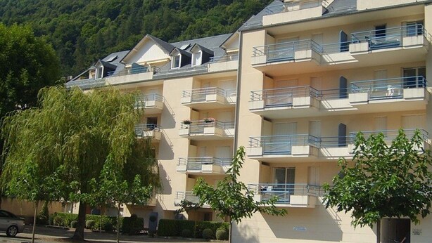 Un hôtel à plusieurs étages doté de balcons, d’un parking et surplombant une colline boisée.