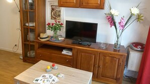 Un salon avec un meuble en bois, une télévision, une table à jeux et un vase rempli de fleurs.