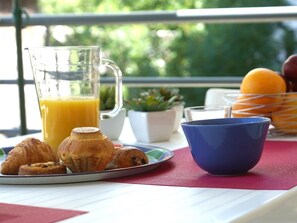 Una colazione con croissant, un bicchiere di succo d'arancia, una tazza blu e un cesto di frutta su un tavolo.