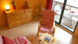 A cozy room with a wooden dresser, a checkered chair, a small table with a chessboard and a glass of juice, and a view of a balcony with white chairs and a table. - Central Luchon Studio for 2 - Balcony - Near Gondola (Bagnères-de-Luchon)