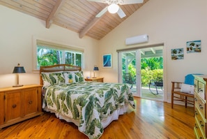 A bedroom with a bed, wooden headboard, two bedside tables, a window, and a sliding glass door leading to a balcony.