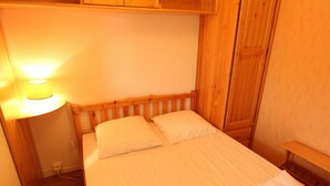 A small, single-bed room with wooden headboard and nightstand, white bedding, and a bedside lamp. - Near Thermal Baths - T2 with Balcony, Parking and WiFi - Pets Allowed (Bagnères-de-Luchon)