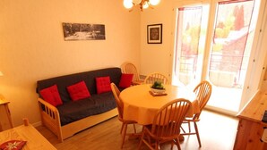 A cozy living area with a dark sofa, red cushions, a round wooden table, and matching chairs. - Near Thermal Baths - T2 with Balcony, Parking and WiFi - Pets Allowed (Bagnères-de-Luchon)