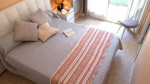 Una cama bien hecha con una colcha estampada, una lámpara de noche y una mesita con un libro.