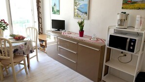 Una cocina funcional con microondas, cafetera y un pequeño comedor con una silla y una mesa.