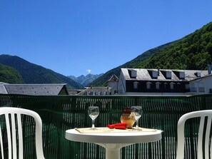 Una mesa con dos copas de vino y una botella, frente a un telón de fondo de montañas y un cielo despejado.