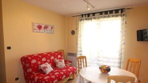 A cozy room with a red sofa, a round dining table, and chairs. - Luchon: Central Apt - Garage, Balcony, 4 Guests, Near Lift & Thermal Baths (Bagnères-de-Luchon)