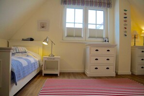 A bedroom with a bed, a nightstand, a dresser, a window with blinds, and a red and white striped rug.