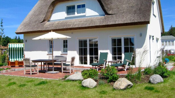 A house with a thatched roof, large windows, and a patio with outdoor furniture. - Windrose, Deutschland (Breege)