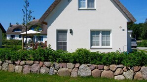 A white house with a stone wall in front, a thatched roof, and a small window. - Windrose, Deutschland (Breege)