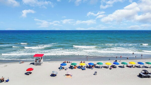 Una playa con sombrillas, sillas y una torre de salvavidas.