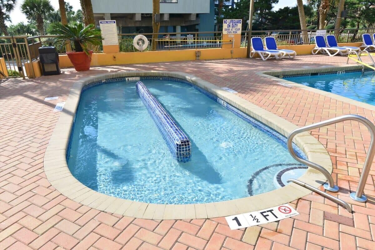 Una piscina con una torre de salvavidas, sillas de descanso y un letrero que indica que no hay salvavidas de servicio.