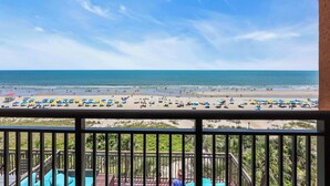 Blick auf einen Strand vom Balkon mit Geländer, Palmen und Strandliegen.