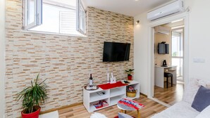 A modern living room with a brick-patterned wall, a mounted TV, a white entertainment unit, and a cozy seating area. - Apartment Vedrana (Dubrovnik)