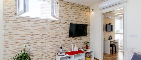 Una sala de estar moderna con pared de ladrillo, televisor montado, mueble blanco para entretenimiento y un rincón de estar acogedor.
