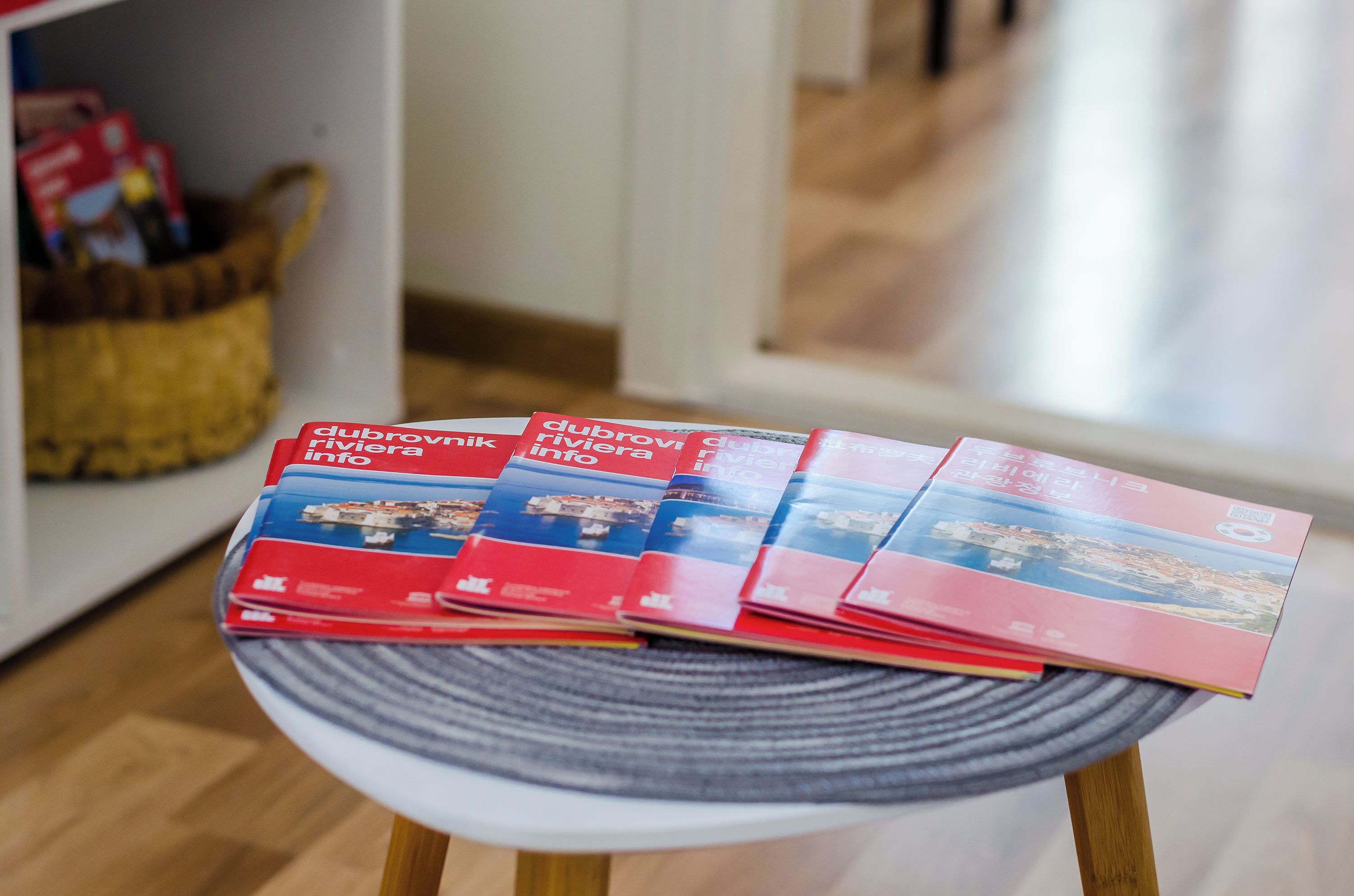 Une pile de brochures est posée sur une table ronde, avec un panier en osier en arrière-plan.