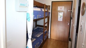 Ein schmaler Flur mit Etagenbetten, einer Holztür mit einem Schild und einem kleinen Schrank mit Toilettenartikeln.