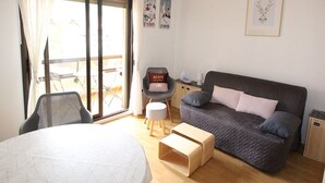 Ein modernes Schlafzimmer mit Bett, Sofa, einem kleinen Tisch und einem Sessel. Ein Fenster mit Vorhängen, ein Poster an der Wand und ein gerahmtes Bild sind ebenfalls zu sehen.