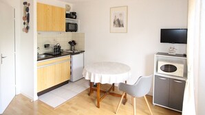 Eine kompakte Küche mit Holzausstattung, einer Mikrowelle, einem kleinen Kühlschrank und einem Esstisch mit zwei Stühlen.