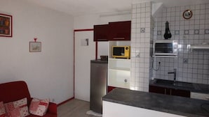 A compact living space with a kitchenette, a red sofa, and a white chair.