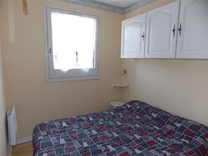 A bedroom with a bed, a window, a white wardrobe, and a small bedside table.