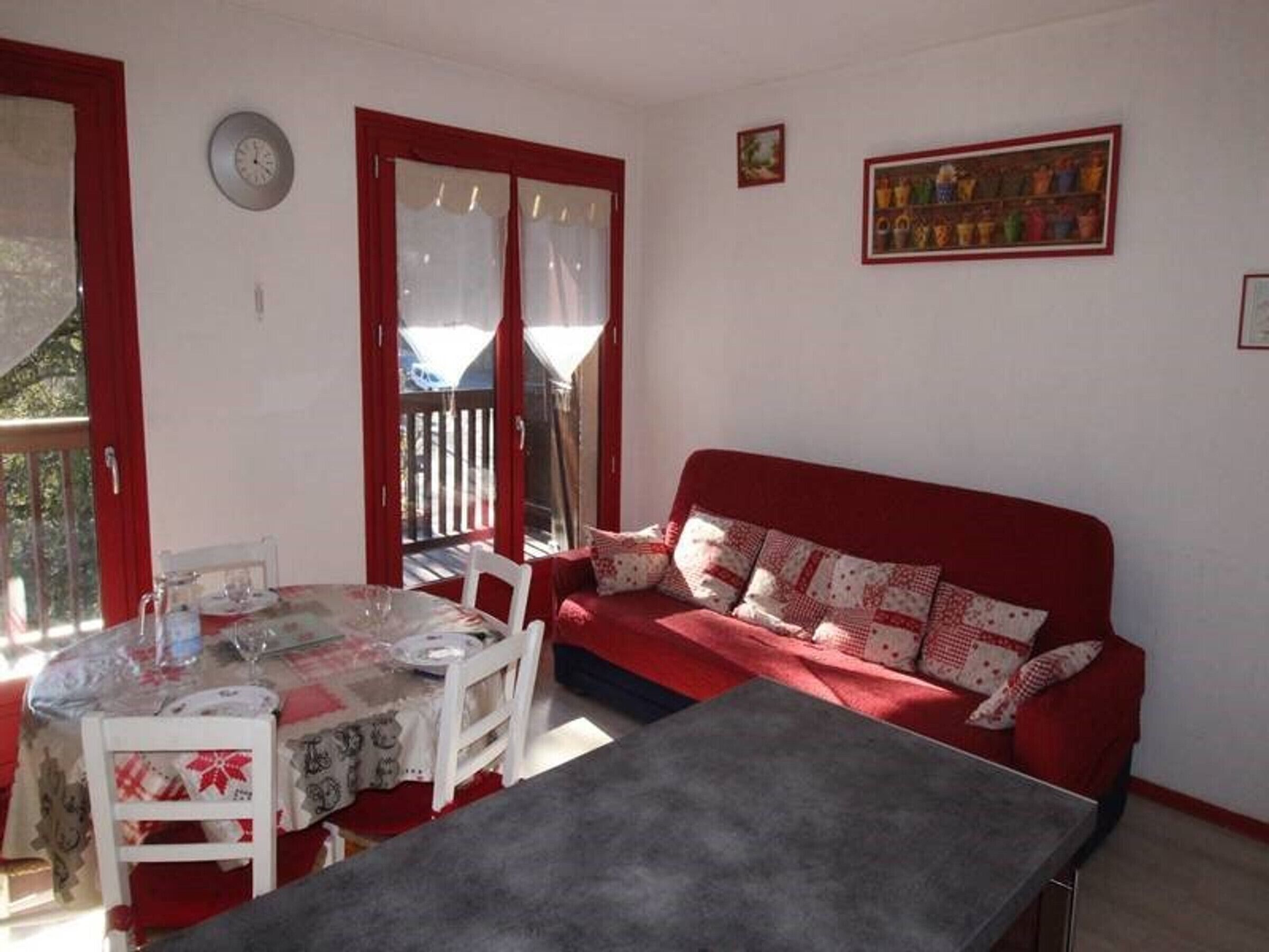 A cozy room with a red sofa, a dining table with chairs, and a large window with curtains.