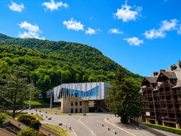 A modern building with a unique geometric facade, surrounded by lush green hills and a clear blue sky.