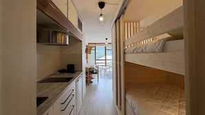Une cuisine compacte, dotée de meubles en bois et d’une cuisinière intégrée, qui donne sur un coin repas avec une table et des chaises.