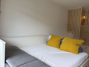 A bed with a white mattress and two pillows, a grey blanket, and a white headboard.